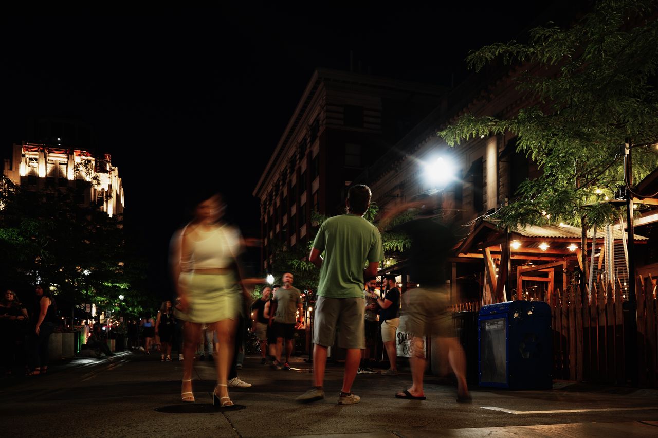 A lively street at night with people walking, capturing motion blur and urban nightlife atmosphere.