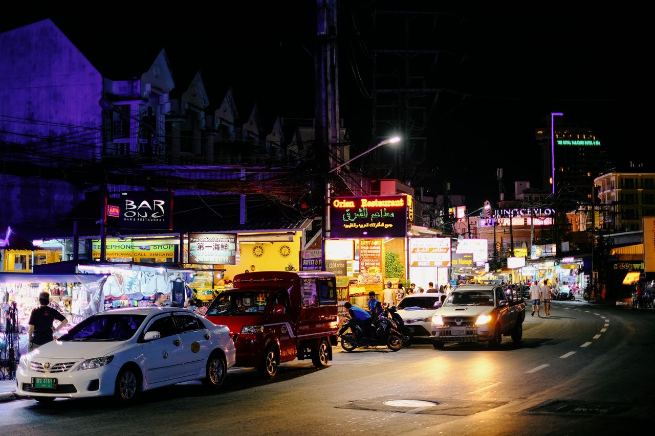 Bustling night scene on a lively street in Bangkok, lit by neon signs and crowded with traffic.