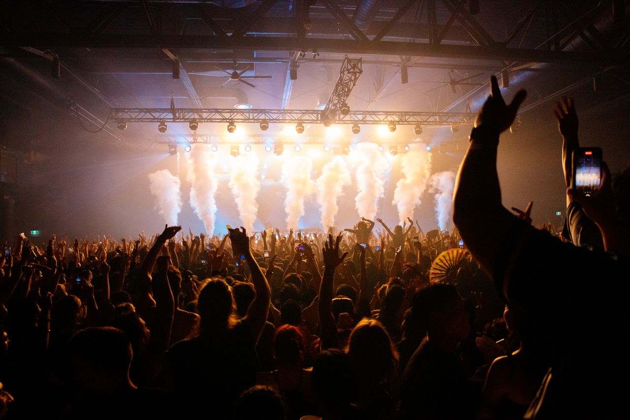 Energetic crowd enjoying a concert with dynamic lighting and smoke effects in an indoor venue.