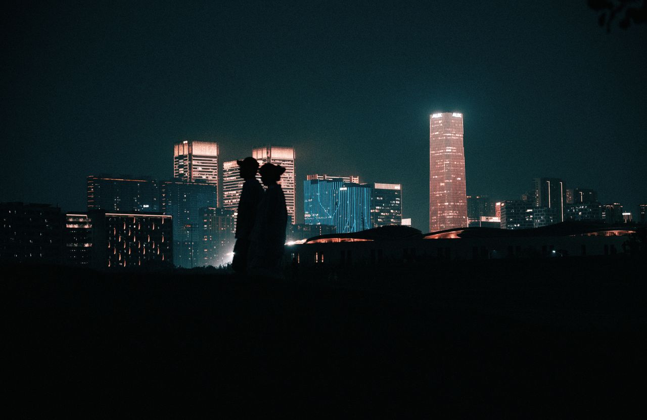 A romantic silhouette of a couple against a vibrant city skyline at night.