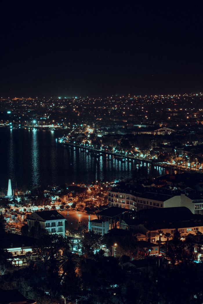 A stunning aerial view of a coastal cityscape illuminated by city lights at night.